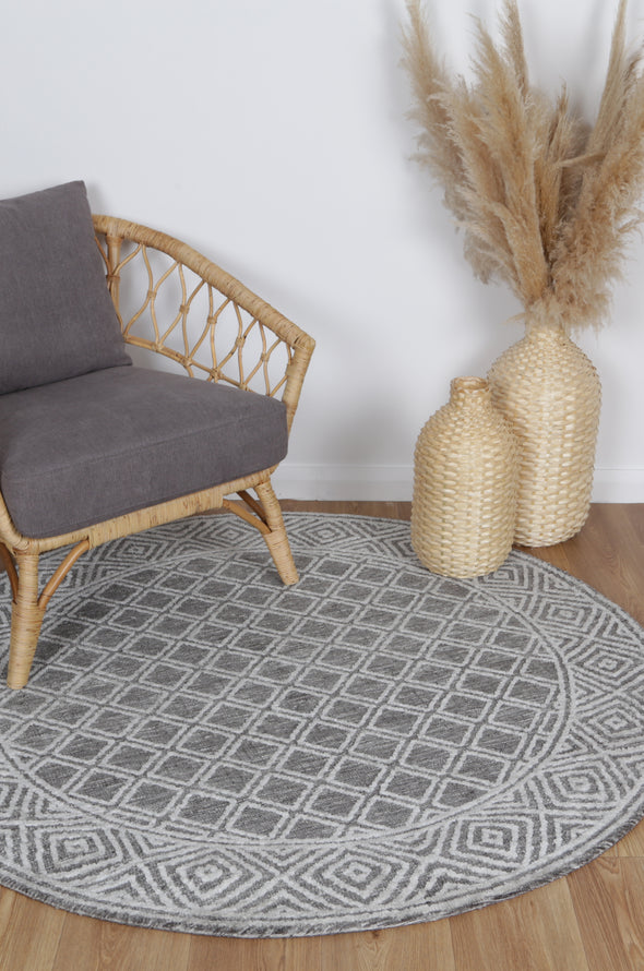 Alayah Diamond Trellis Charcoal circle Rug on light flooring with wicker vase rattan chair