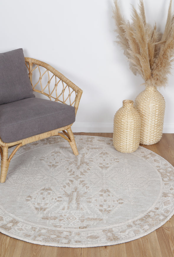 Alayah Ornamental Cream Round Rug on natural wooden floring with grey chair and wicker accessories