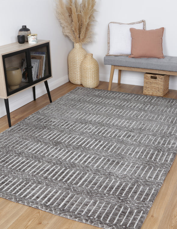 Alayah Geometric charcoal Rug on natural flooring with grey bench wicker baskets and blush cushions