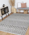 Alayah Tessellations silver Rug in living room with light flooring and a grey chair and woven accessories