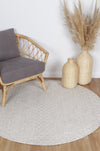Alayah Tessellations ivory circle Rug on natural flooring with grey chair and wicker accessories