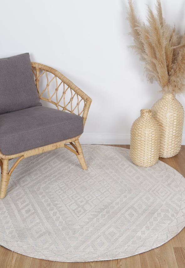 Alayah Zalij ivory circle Rug in living room with wooden floors, a grey arm chair and natural accessories