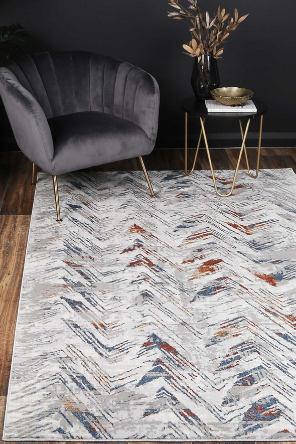 Almada silver and Multicoloured herringbone Rug, with charcoal velvet arm chair, dark walls on natural timber flooring