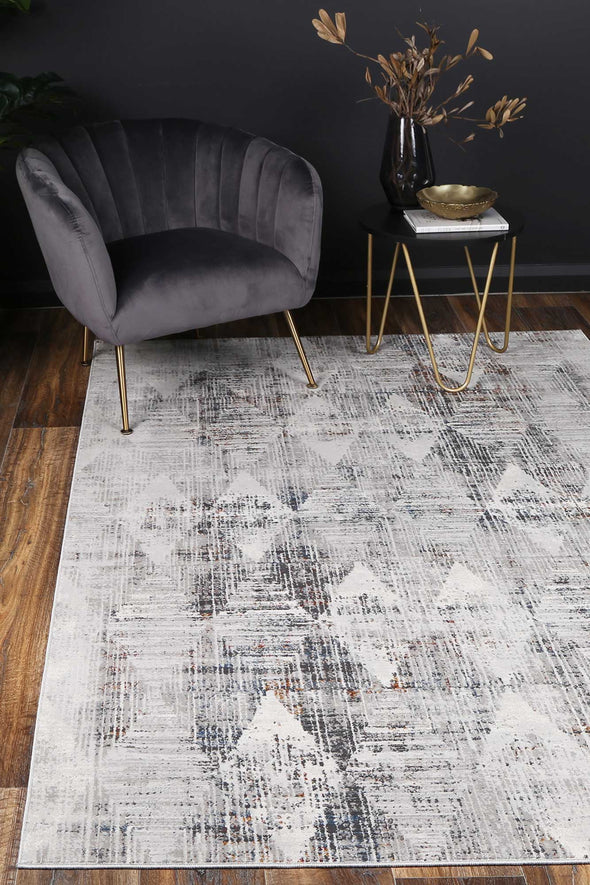 Almada silver and multicoloured Diamond Transitional Rug with charcoal chair on wooden flooring, dried flowers and gold accessories