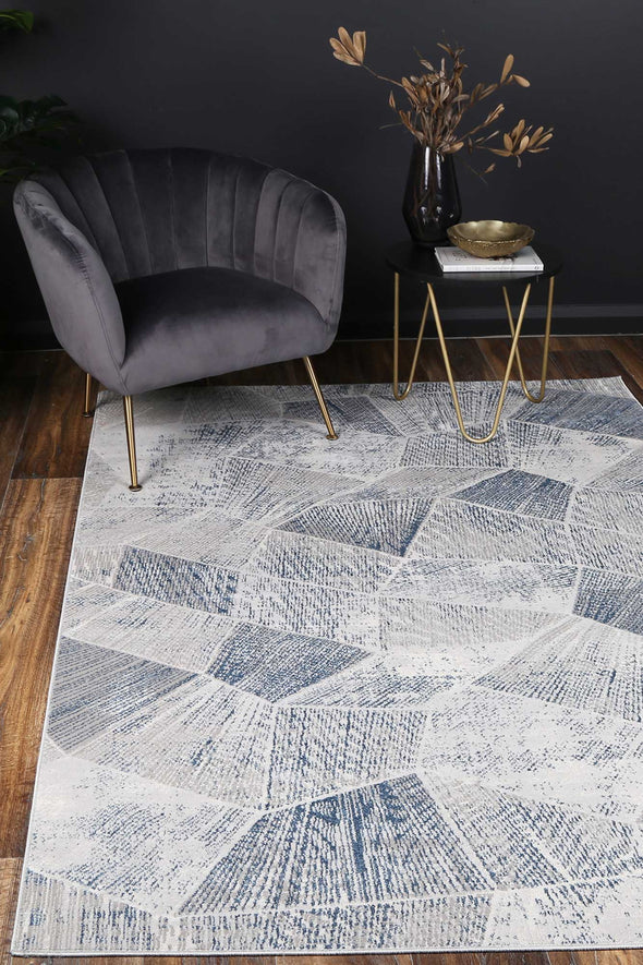 Almada Teal and silver Tiled Geometric Rug on timner floors with charcoal velvet arm chair, dark walls and gold accessories
